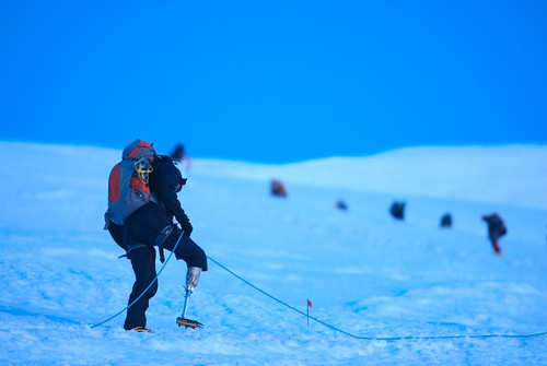 Climber with prosthetic leg ascending snowy mountain.