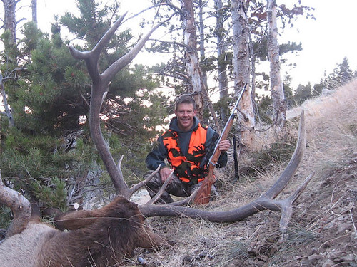 Hunter posing with elk in forest clearing.
